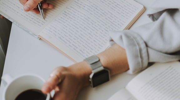 Homepage canva   person writing on notebook while holding coffee mug