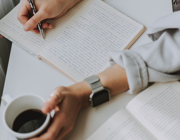 Large canva   person writing on notebook while holding coffee mug